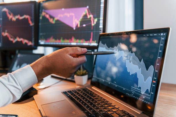 istock Close up view. Young businessman in formal clothes is in office with multiple screens 1369748014
