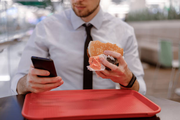 istock Office worker snacking on burger in mall, surfing the internet in a mobile while eating 1369748152