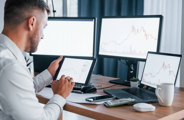 istock Modern technologies. Young businessman in formal clothes is in office with multiple screens 1369748416