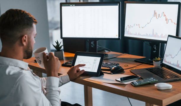 istock Looking at information. Young businessman in formal clothes is in office with multiple screens 1369748471