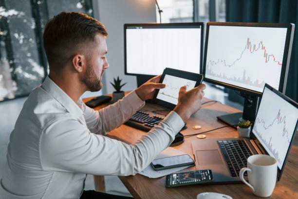 istock Looking at information. Young businessman in formal clothes is in office with multiple screens 1369748472