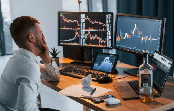 istock With alcohol. Young businessman in formal clothes is in office with multiple screens 1369748810
