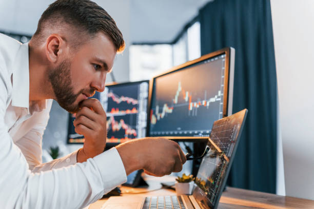 istock Analyzing information. Young businessman in formal clothes is in office with multiple screens 1369749626