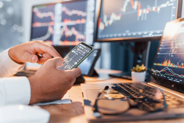 istock Side view. Young businessman in formal clothes is in office with multiple screens 1369749784
