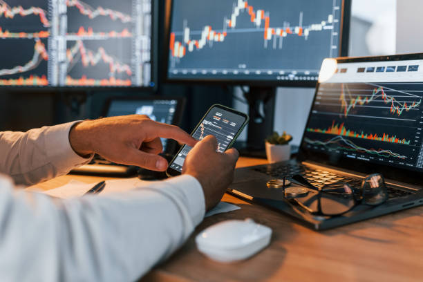 istock Side view. Young businessman in formal clothes is in office with multiple screens 1369749786