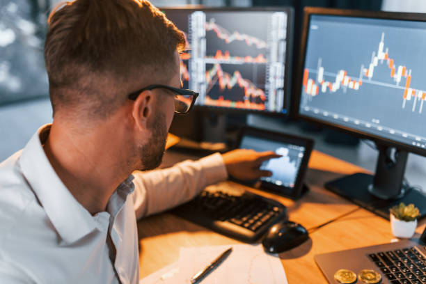 istock Many monitors. Young businessman in formal clothes is in office with multiple screens 1369750090