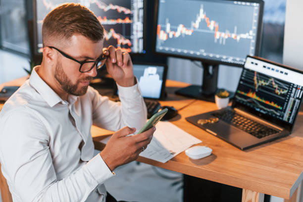 istock In formal clothes. Young businessman is in office with multiple screens 1369750168