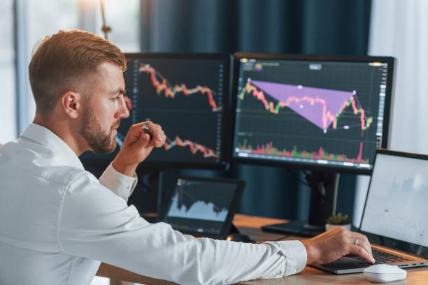 istock Graphs is going down. Young businessman in formal clothes is in office with multiple screens 1369750732