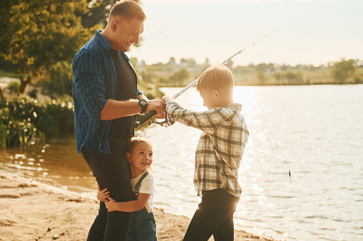 Dad shows his son how to hold the spinning and spin the reel. Fishing training on a pond or river. Caring parent concept. Father and son fishing.