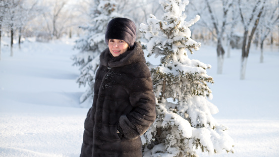 A brunette woman in winter clothes walks through the winter forest.