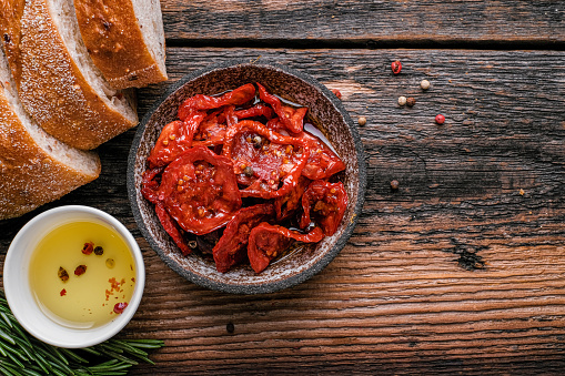 Sun dried tomatoes  on wooden bowl, rustic wooden background. Dried tomatoes with olive oil, salt, herbs and garlic recipe.  Top view,  copyspace.