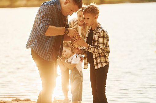 Illuminated by sunlight. Father and mother with son and daughter on fishing together outdoors at summertime.