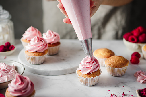 Mujer haciendo glaseado en cupcakes con crema batida rosa photo