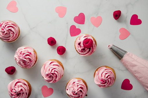 Preparing raspberry cupcakes with paper hearts on marble table