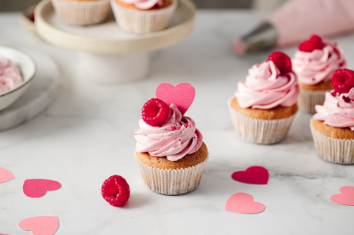 Freshly made raspberry cupcakes on kitchen counter. Delicious looking pink cupcakes with raspberry and paper heart topping.