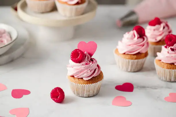 Freshly made raspberry cupcakes on kitchen counter. Delicious looking pink cupcakes with raspberry and paper heart topping.