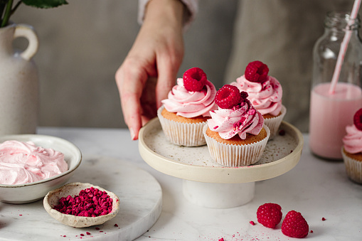 Close-up of a woman hand holding pink cupcakes in a tray. Female preparing delicious raspberry cupcakes in kitchen.