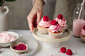 Close-up of woman with delicious raspberry cupcakes in kitchen
