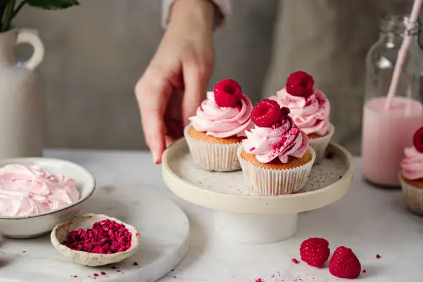 Photo of Close-up of woman with delicious raspberry cupcakes in kitchen