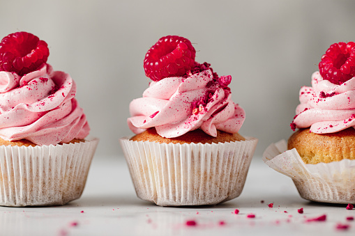 Close-up of raspberry cupcakes in a row on the kitchen counter. Delicious pink cupcakes with red powdered sugar and berry toppings.