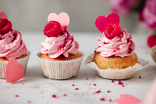 Close-up of raspberry cupcakes in a row on the kitchen counter. Delicious pink cupcakes with raspberry toppings and paper hearts.