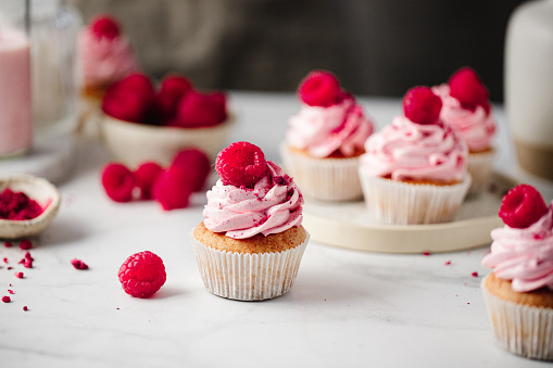 Close-up of delicious pink cupcakes with raspberry toppings on the table. Freshly made raspberry cupcakes on the kitchen table.