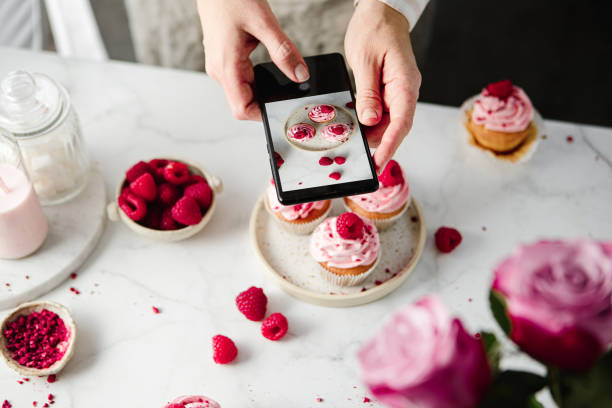 woman taking a photo of pink cupcakes with smartphone - muffin blueberry muffin blueberry butter imagens e fotografias de stock