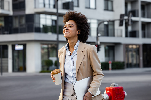 Portrait of a businesswoman on the street, walking and carrying laptop and a coffee