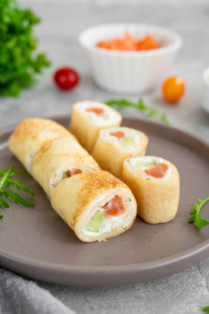 istock Thin pancake rolls or crepes rolls with smoked salmon, cream cheese, cucumber and dill on a gray concrete background. Selective focus. 1369760028