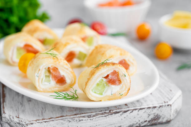 istock Thin pancake rolls or crepes rolls with smoked salmon, cream cheese, cucumber and dill on a gray concrete background. Selective focus. 1369760107