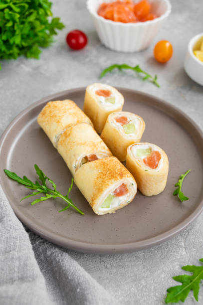 istock Thin pancake rolls or crepes rolls with smoked salmon, cream cheese, cucumber and dill on a gray concrete background. Selective focus. 1369760108