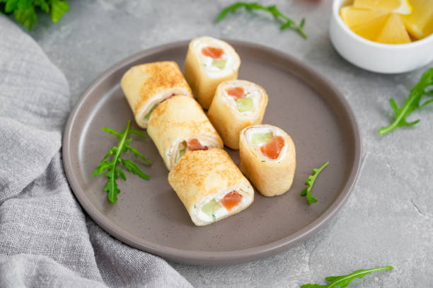 istock Thin pancake rolls or crepes rolls with smoked salmon, cream cheese, cucumber and dill on a gray concrete background. Selective focus. 1369760627