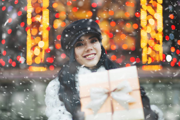 Joyful young woman receiving gift at the holiday fair during snowfall. Empty space