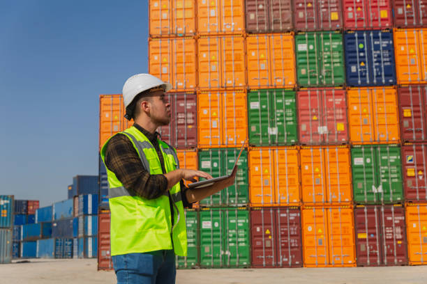 istock Engineer man with yellow crash helmet and worker west checking cargo freights in front of colorful cargo container stacks in shipping port 1369763688