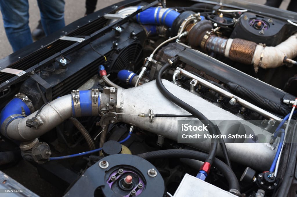 Sports car engine with turbine. An open race car hood on a pit stop while racing on a race track. Motor with turbocharger. Sports car engine with turbine. An open race car hood on a pit stop while racing on a race track. Motor with turbocharger. Boos and tunning. Supercharged Engine Stock Photo