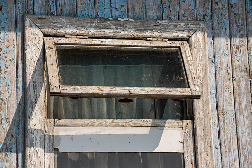The window of the old wooden log house on the background of wooden walls.