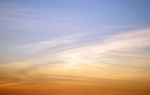 Skyscape at sunset of simple gradient colors of orange and white clouds against blue sky