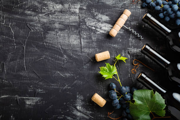 istock Wine bottles grapes, grape bunches with leaves and vines corkscrew wine corks on dark rustic concrete background. Flat lay wine composition on black stone table with copy space. 1369766258
