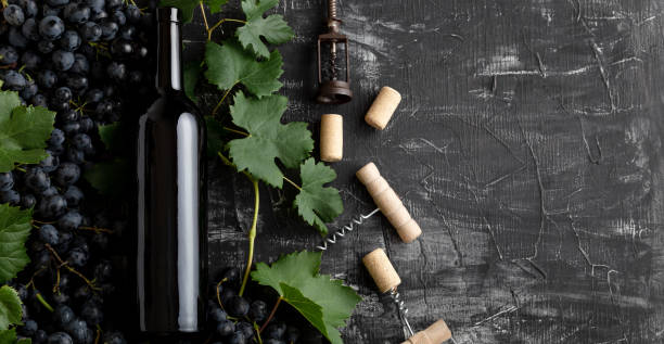 istock Red Wine bottle grape bunches with leaves and vines corkscrew on dark rustic concrete background. Flat lay wine composition Red Wine bottle on black stone table. Long web banner with copy space. 1369766271
