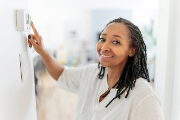 A frican woman lady adjusting the climate control panel on the wall wall thermostat stock photo