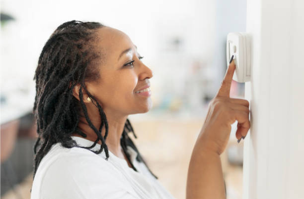 A frican woman lady adjusting the climate control panel on the wall wall thermostat An african woman lady adjusting the climate control panel on the wall wall thermostat thermostat stock pictures, royalty-free photos & images