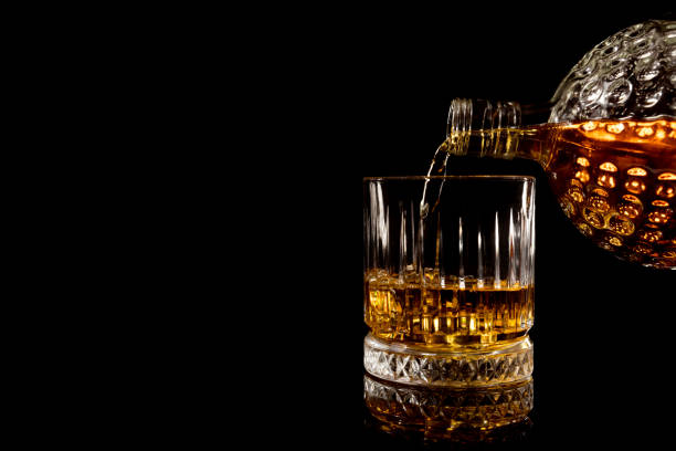 pouring glass of whiskey on black background stock photo