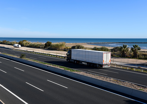 Semi-trailer truck driving along highway. Traffic on motorway and road near sea. Logistics of transportation and delivery of goods. Services and Transport logistics in a pandemic in Europe.