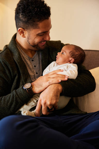 Smiling dad sitting at home and holding his baby boy in his arms stock photo