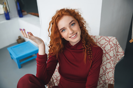 Portrait of a smiling young redheaded woman sitting and looking at camera indoors