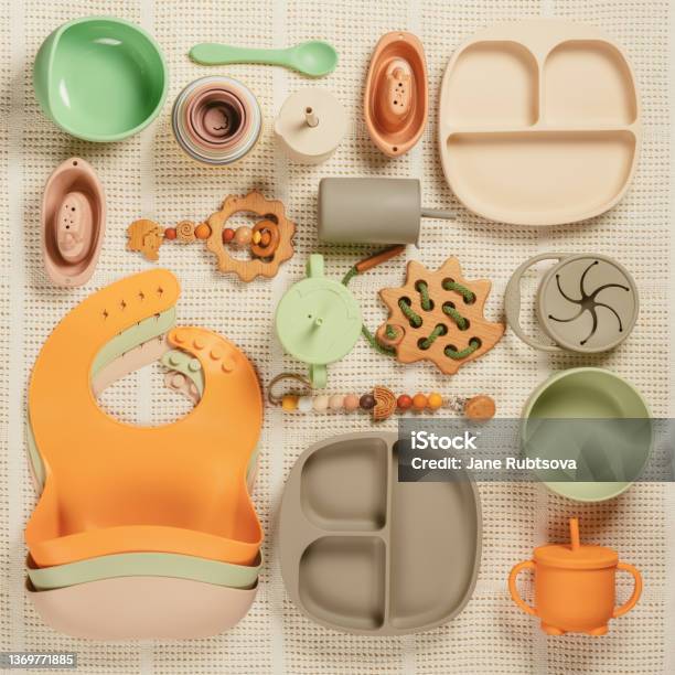 Pastel Silicone Set Of Tableware Cutlery Bibs Accessories And Wooden Toys For Children On White Cloth Background Stock Photo - Download Image Now