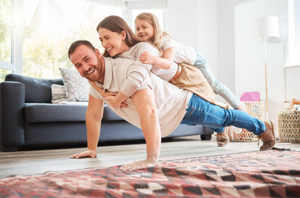 Shot of a young father doing pushups with his wife and daughter on his back at home He lifts them up when they're feeling down push ups stock pictures, royalty-free photos & images