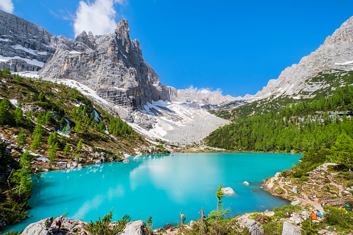 Hikers resting at the shore of the Lago di Sorapiss, famous for its turquoise waters. Over the lake looms the imposing bulk of the Dito di Dio (Finger of God) of the Sorapiss mountain, Dolomites