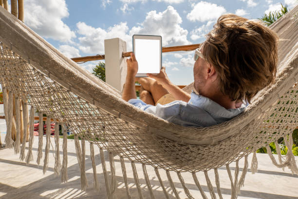 istock Young man relaxing in an hammock on a balcony using a digital tablet 1369774912