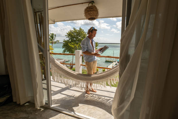 jeune homme se relaxant dans un hamac sur un balcon à l’aide d’une tablette numérique - reading beach e reader men photos et images de collection